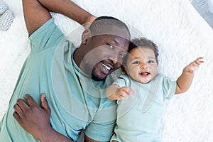 Happy smiling African american dad with baby son on bed at home cuddle, happy family, father`s day