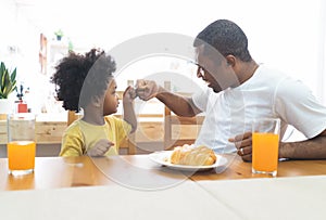 Happy smiling African American family fist bumping while eating breakfast on the table at home together. Family enjoy meal. Happy