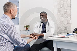 A happy smiling African-American male doctor supports the patient during the consultation, sitting at the table