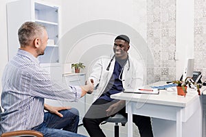 A happy smiling African-American male doctor talks to a patient while sitting at a table.