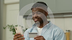 Happy smiling African American man with phone and credit card shopping online internet purchase buy goods distant