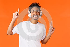Happy smiling african-american man in white t-shirt, looking up and smiling as listening music using headphones, dancing