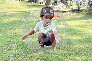 Happy smiling African boy blowing soap bubbles at green garden. Child having fun with bubble in summer park. Kid spending time
