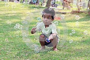 Happy smiling African boy blowing soap bubbles at green garden. Child having fun with bubble in summer park. Kid spending time