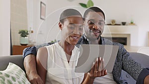 Happy smiling african couple doing video call with digital tablet at home
