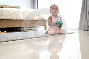 Happy smiling African cute toddle baby infant kid holding toy while crawling on floor in bedroom at home. Happy child with