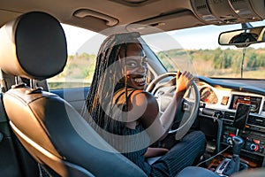 Happy smiling african girl in black striped clothes is driving a car