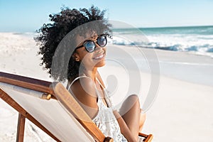 Happy smiling african woman sitting on deck chair at beach