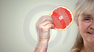 Happy smiling aged woman showing slice of juicy grapefruit, half-face closeup