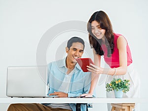 Happy smiling Asian business couple, young man and woman, colleagues using tablet and laptop computer.