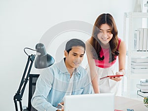 Happy smiling Asian business couple, young man and woman, colleagues using tablet and laptop computer.