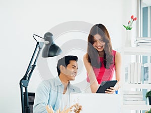 Happy smiling Asian business couple, young man and woman, colleagues using tablet and laptop computer.