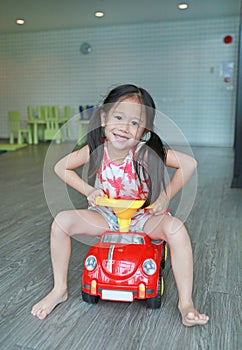 Happy smiling Asian child girl driving car toy at playroom