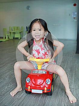 Happy smiling Asian child girl driving car toy at playroom