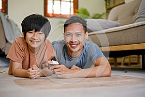 Happy and smiling Asian dad and son laying on the living room floor together
