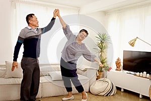 Happy smiling Asian elderly couple dancing in living room, romantic senior lover having fun together at home, mature retired