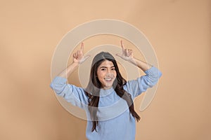 Happy smiling Asian female in sweater shirt pointing fingers up in empty copy space - insert any advertising and promo.