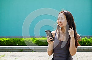 Happy smiling asian girl with mobile phone reads message , blue background.