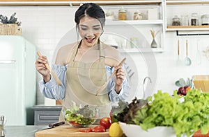 Happy smiling asian housewife in apron cooking salad in kitchen. woman healthy cooking concept
