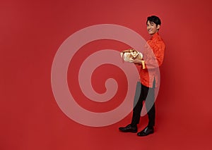 Happy smiling Asian man in red traditional costume giving gold gift box for bless chinese new year 2024 isolated on red copy space