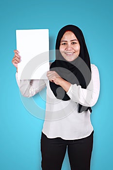 Happy smiling Asian muslim woman looaking at camera while showing blank empty white paper