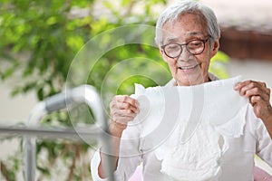 Happy smiling asian senior woman holding disposable diaper for adult,looking at nappy pamper with satisfaction,old elderly patient photo