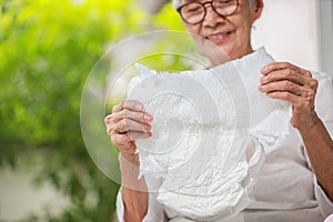 Happy smiling asian senior woman showing disposable diaper for adult,looking at nappy pamper with satisfaction,old elderly patient photo