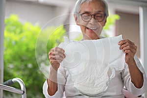 Happy smiling asian senior woman showing disposable diaper for adult,looking at nappy pamper with satisfaction,old elderly patient photo