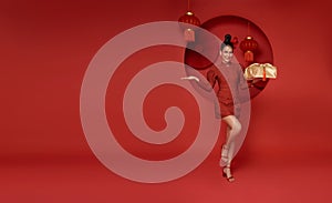 Happy smiling Asian woman in red traditional costume giving gold gift box on decoration traditional for chinese new year header