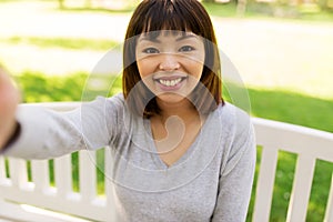 Happy smiling asian woman taking selfie at park