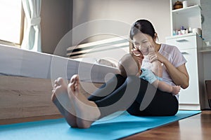 Happy smiling Asian young mother in sportswear playing and holding small baby son feet while practicing yoga in bedroom