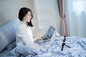 Happy smiling asian young woman with laptop computer and mobile phone having video call in the bedroom