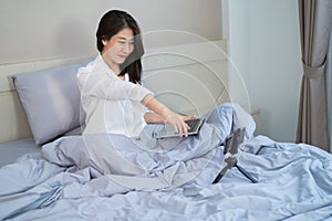 Happy smiling asian young woman with laptop computer and mobile phone having video call in the bedroom