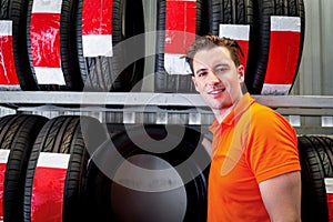 Happy smiling auto handsome mechanic standing with stack wheel tires at vehicle repair service shop, man working in garage, car