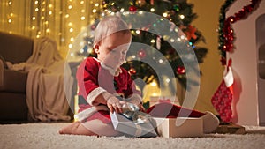 Happy smiling baby boy playing and opening Christmas gift box on Xmas eve. Families and children celebrating winter