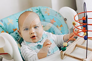 Happy smiling baby boy playing toys in high chair at home