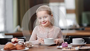 Happy smiling baby girl posing holding cup of tea sitting at table. Close up shot on 4k RED camera