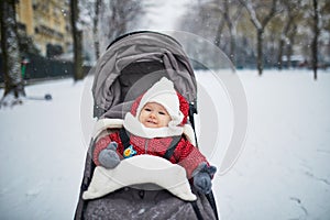 Happy smiling baby girl in stroller in Paris day with heavy snow