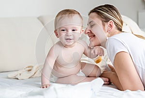 Happy smiling baby siting with his mother on bed at bedroom