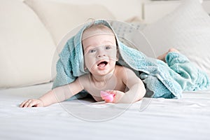 Happy smiling baby under blue towel crawling on bed with white s
