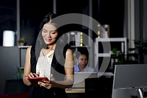 Happy smiling beautiful Asian business woman officer working at digital tablet, employee working hard overtime at night in office