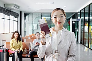 Happy smiling beautiful Asian woman traveler showing passport at airport terminal with blurred background of passenger waiting for