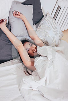 Happy smiling beautiful long hair asian girl young woman lying down in bed, cozy morning