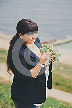 Happy smiling beautiful overweight young woman in dark blue jacket outdoors near to sea with flowers. Confident fat young woman.