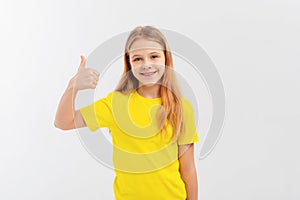 Happy smiling beautiful teen girl showing thumb up gesture, standing over white background in yellow tshirt