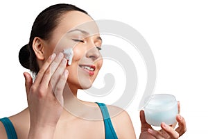 Happy smiling beautiful woman applying moisturizer cream on the face