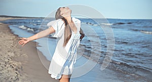 Happy smiling beautiful woman is on the ocean beach in a white summer dress, open arms