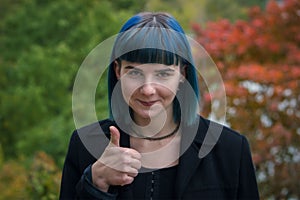 Happy smiling beautiful young businesswoman in black showing thumbs up gesture, on autumn forest background