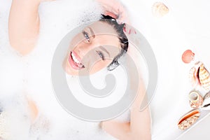 Happy smiling beautiful young woman with blue eyes plunged into the foam, showing tongue & looking at camera portrait
