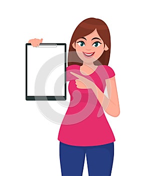 Happy smiling beautiful young woman holding / showing a blank clipboard and pointing towards.